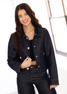 Woman wearing a dark denim jacket with gold buttons on a white background