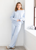 Woman wearing a light blue loungewear set sitting by a window.