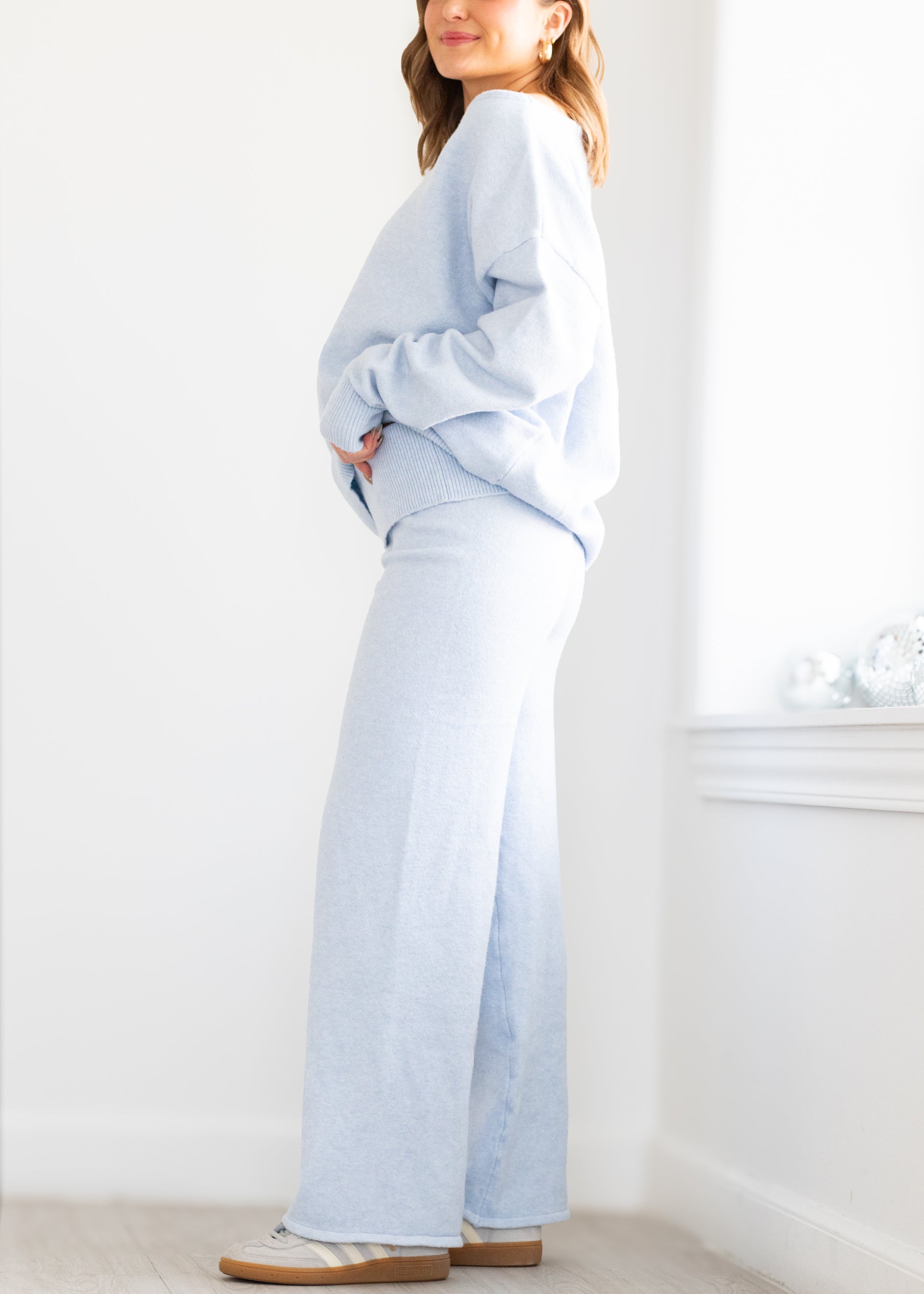 Person wearing a light blue outfit standing in a room with a white wall and window.