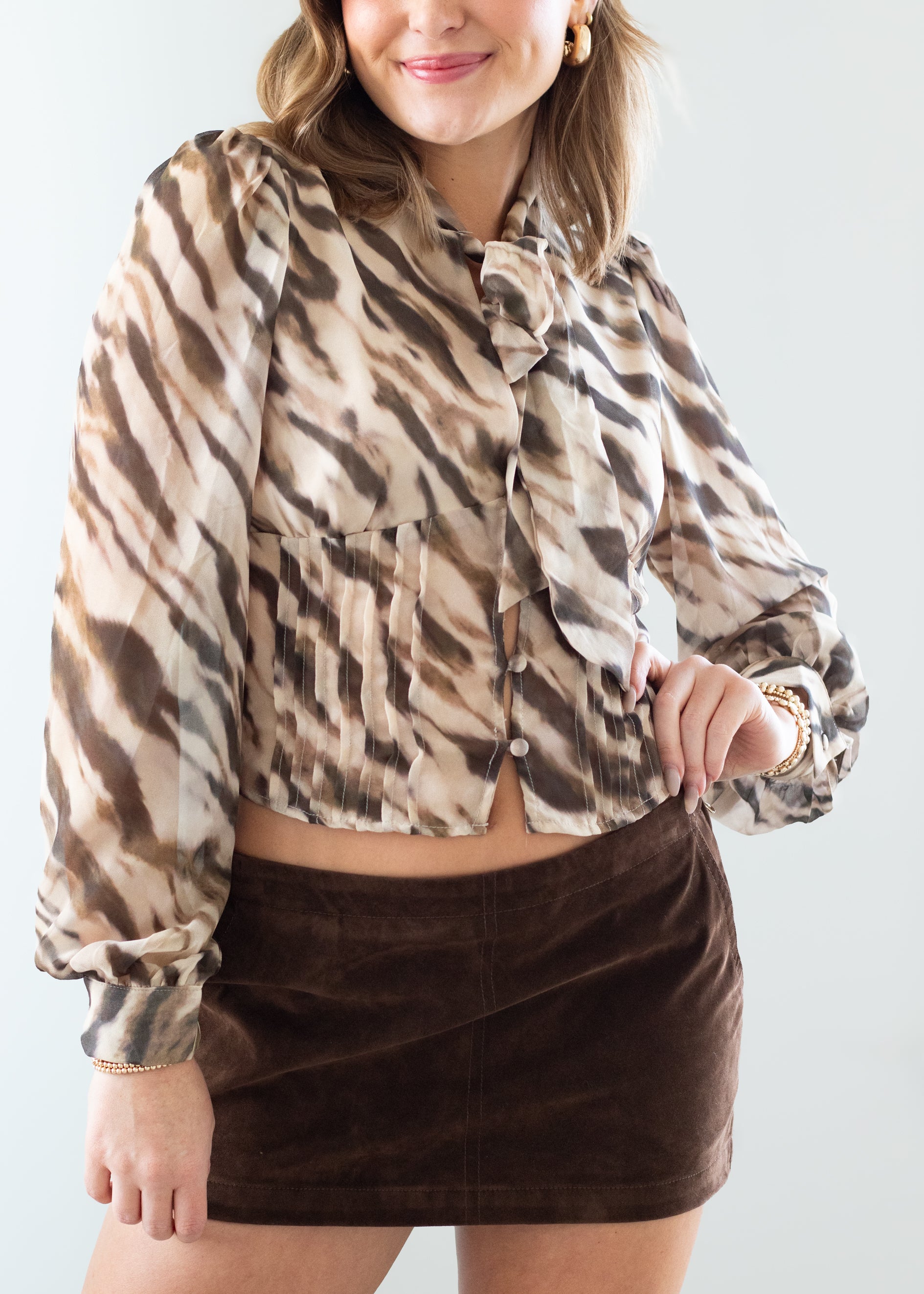 Woman wearing a zebra patterned blouse and brown suede skirt against a white background