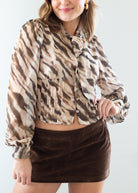 Woman wearing a zebra patterned blouse and brown suede skirt against a white background