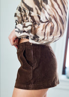 Person wearing a patterned shirt and brown skirt against a neutral background
