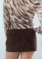 Person wearing a patterned top and brown skirt against a light background