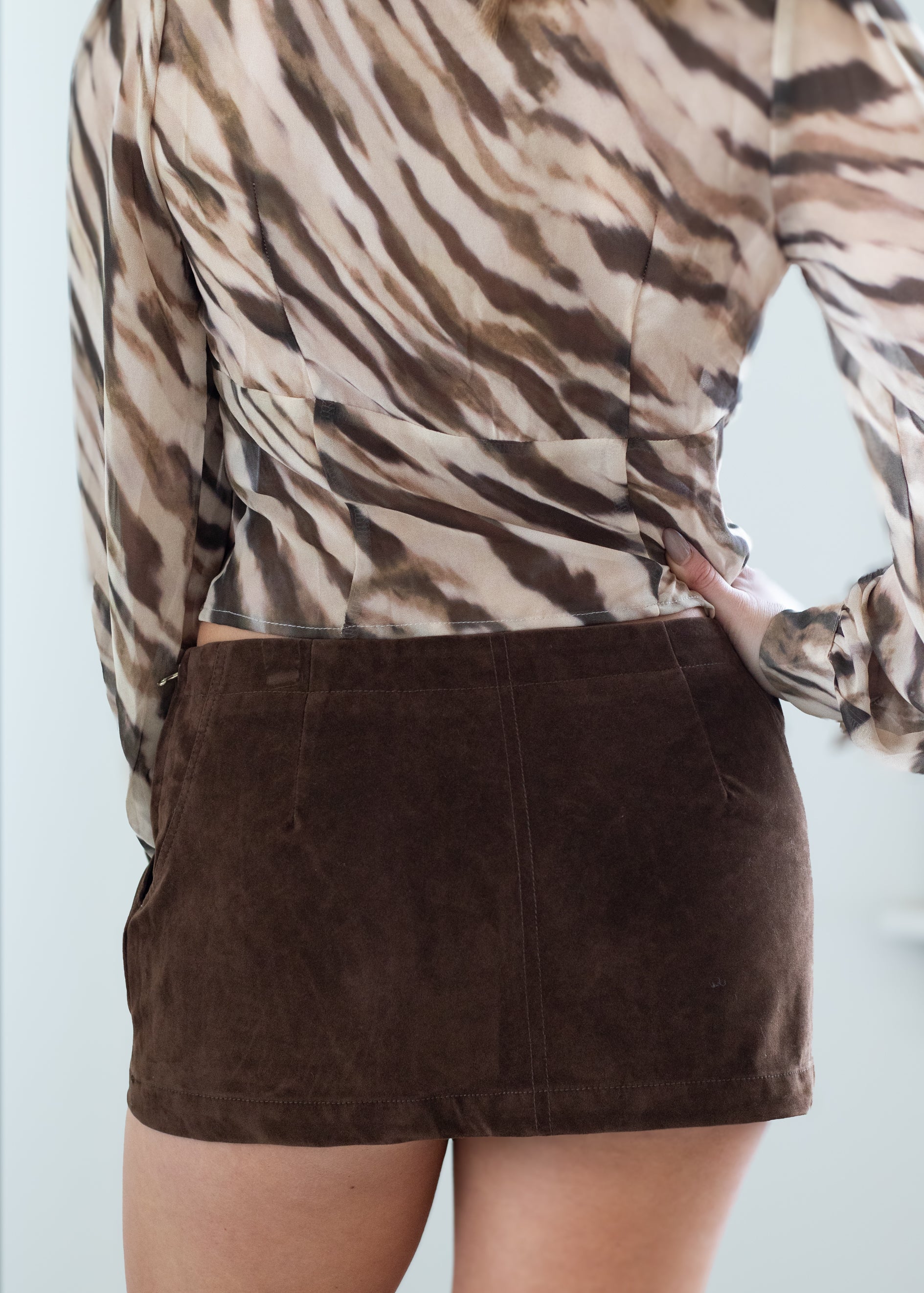 Person wearing a patterned top and brown skirt against a light background