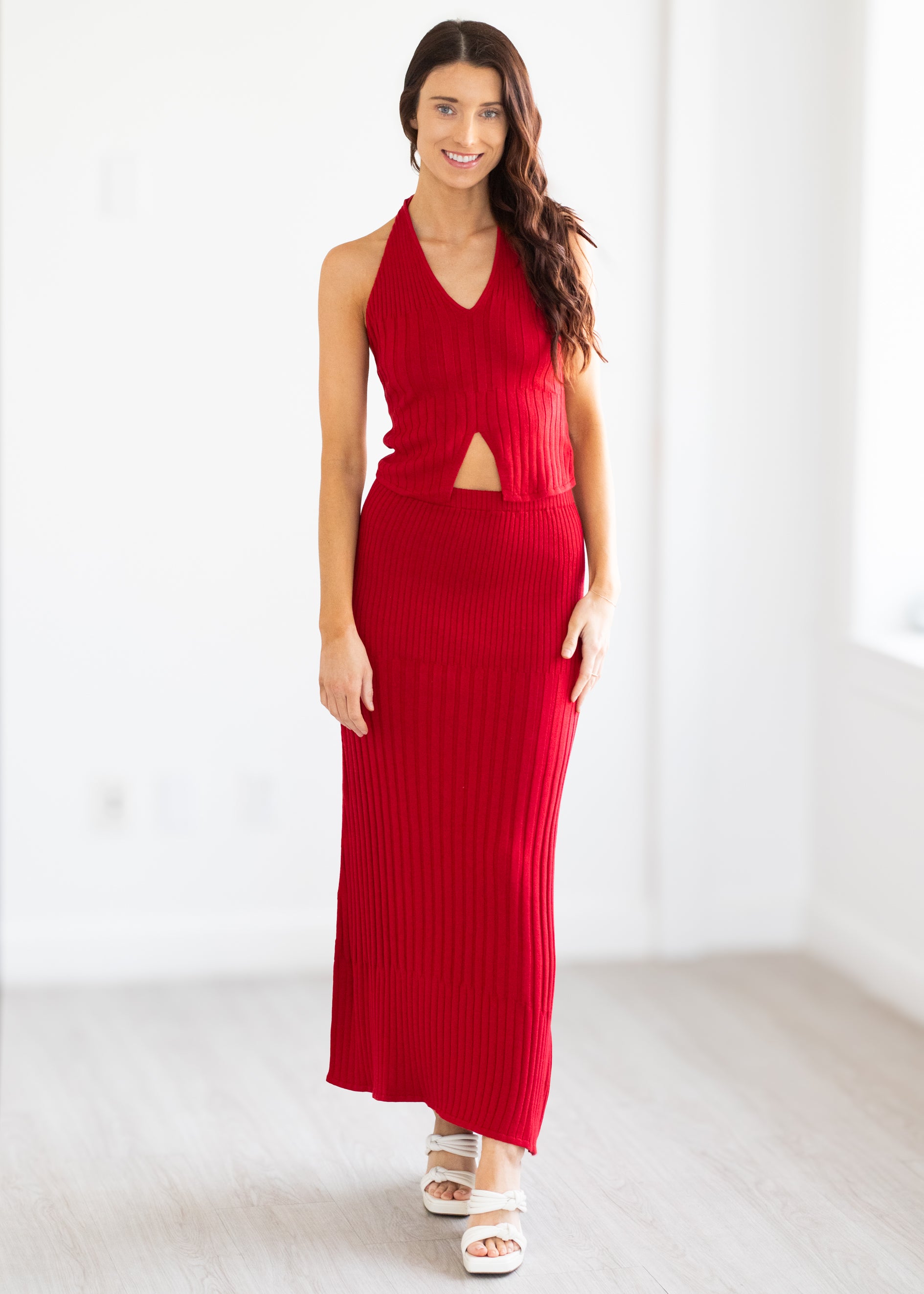Woman wearing a red halter neck top with cut-out details and matching skirt on a white background