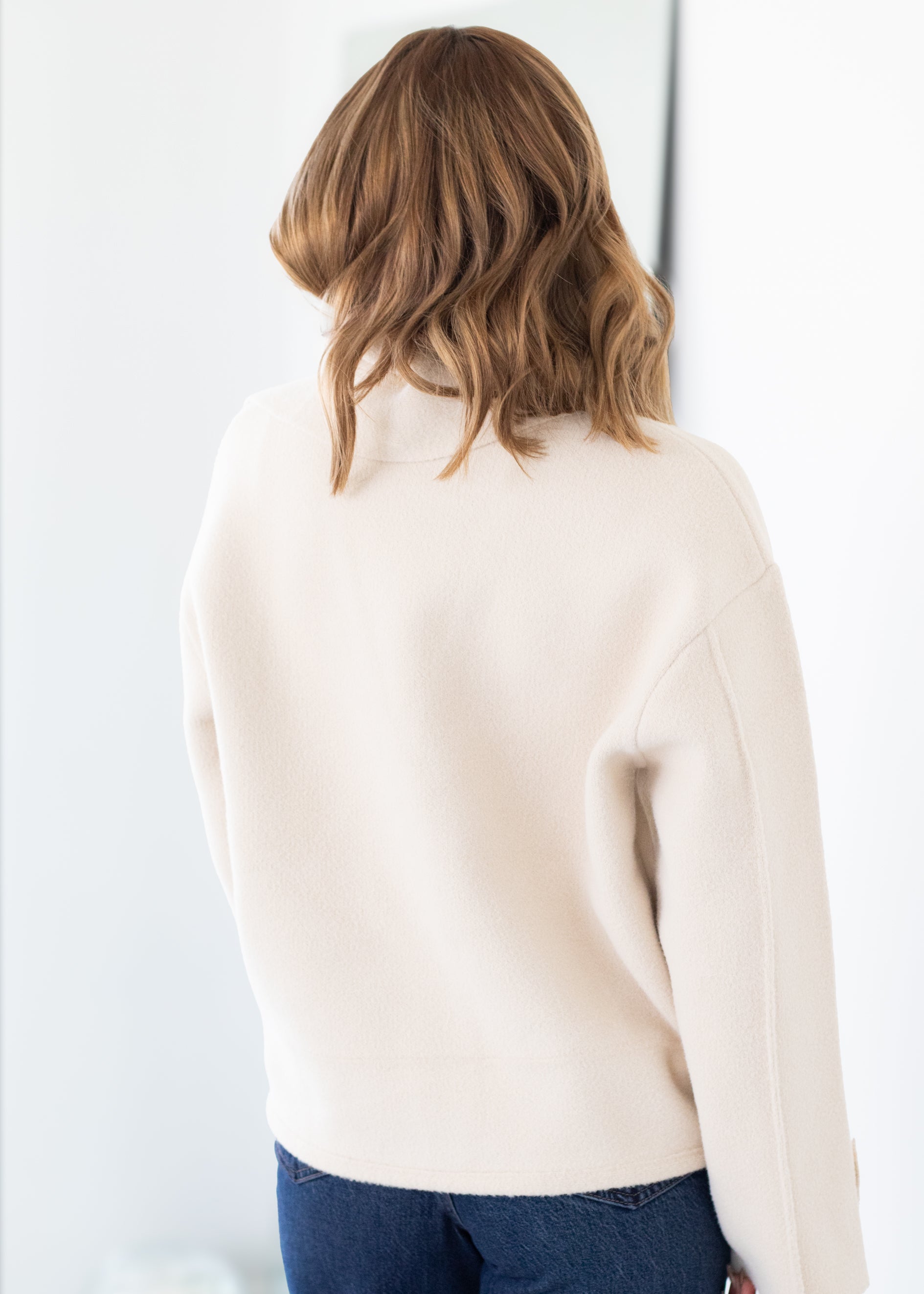 Person wearing a beige sweater and blue jeans against a white background