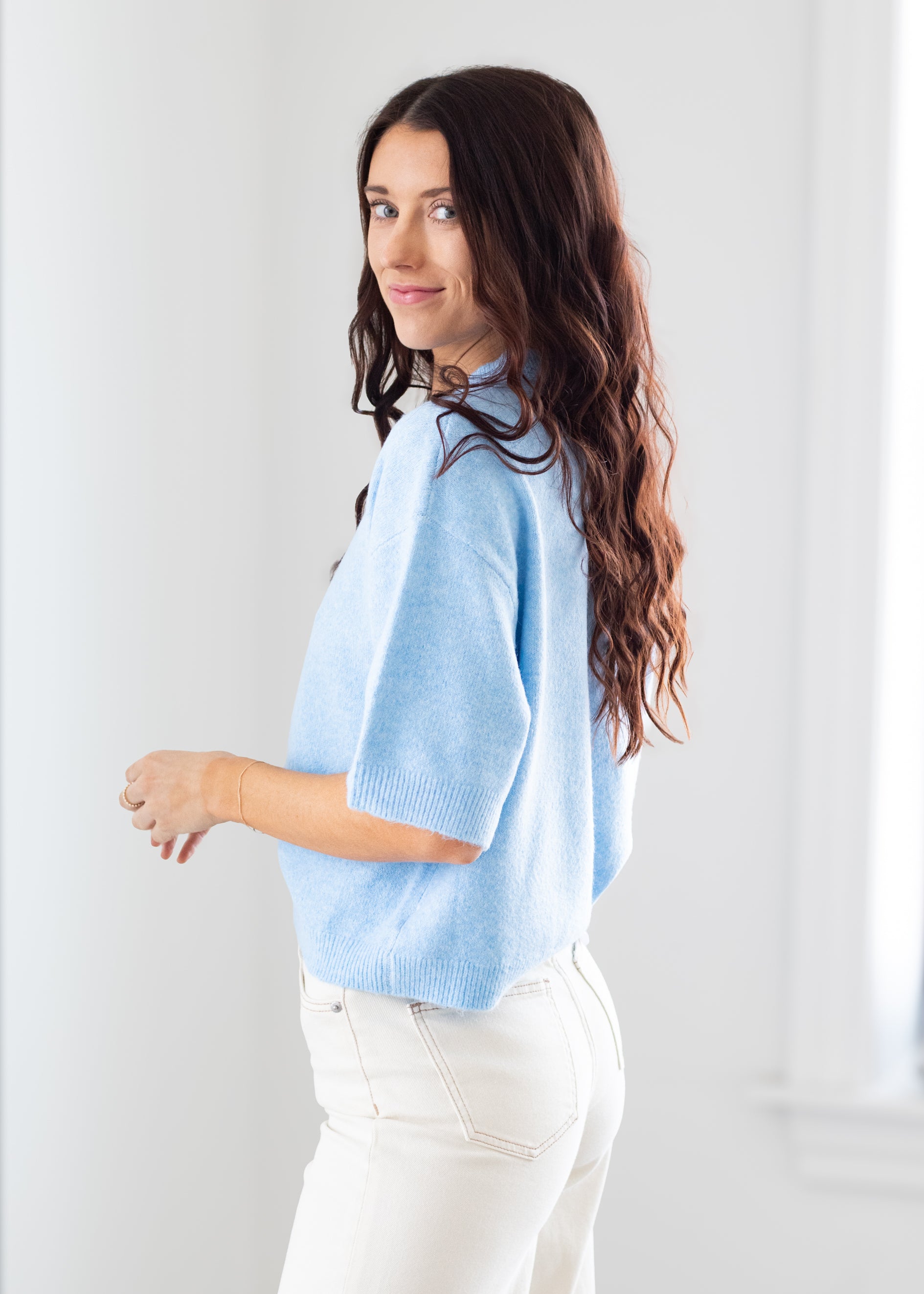 Woman wearing a light blue sweater and white pants against a plain background