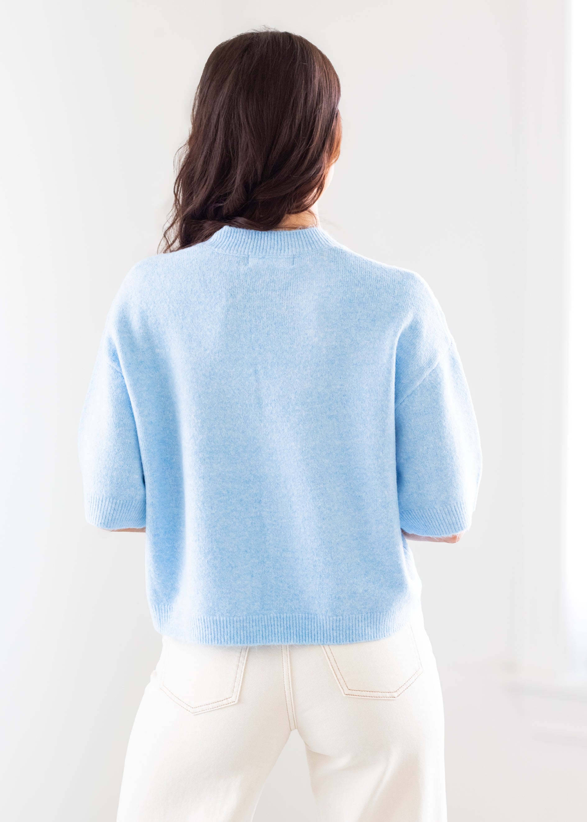 Person wearing a light blue sweater and white pants against a white background