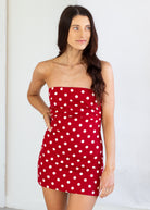 Woman wearing a red strapless dress with white polka dots against a plain background