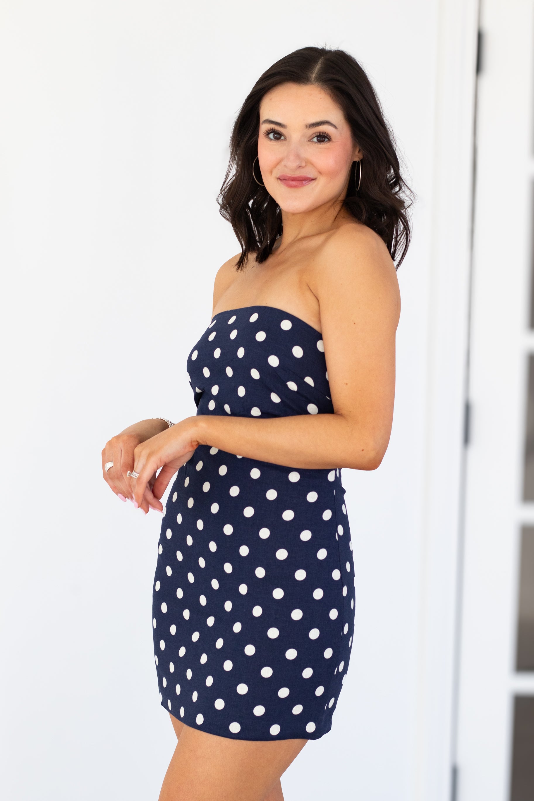 Woman wearing a navy strapless dress with white polka dots against a white background