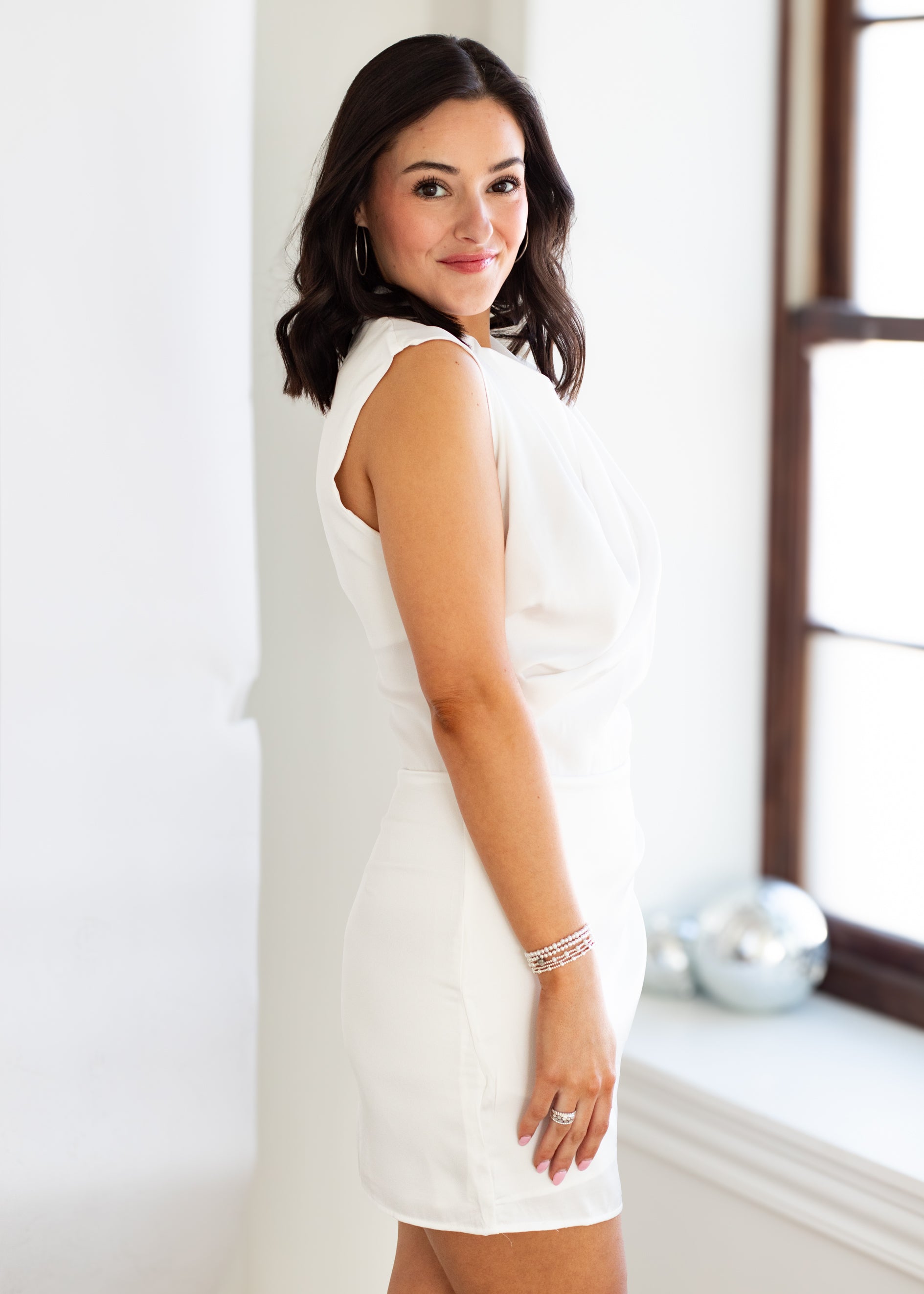 Woman wearing a white dress standing against a light-colored wall.