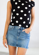 Person wearing a black sleeveless top with white polka dots and a denim skirt on a plain background