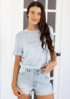 Woman wearing a striped shirt and denim shorts standing against a white door.