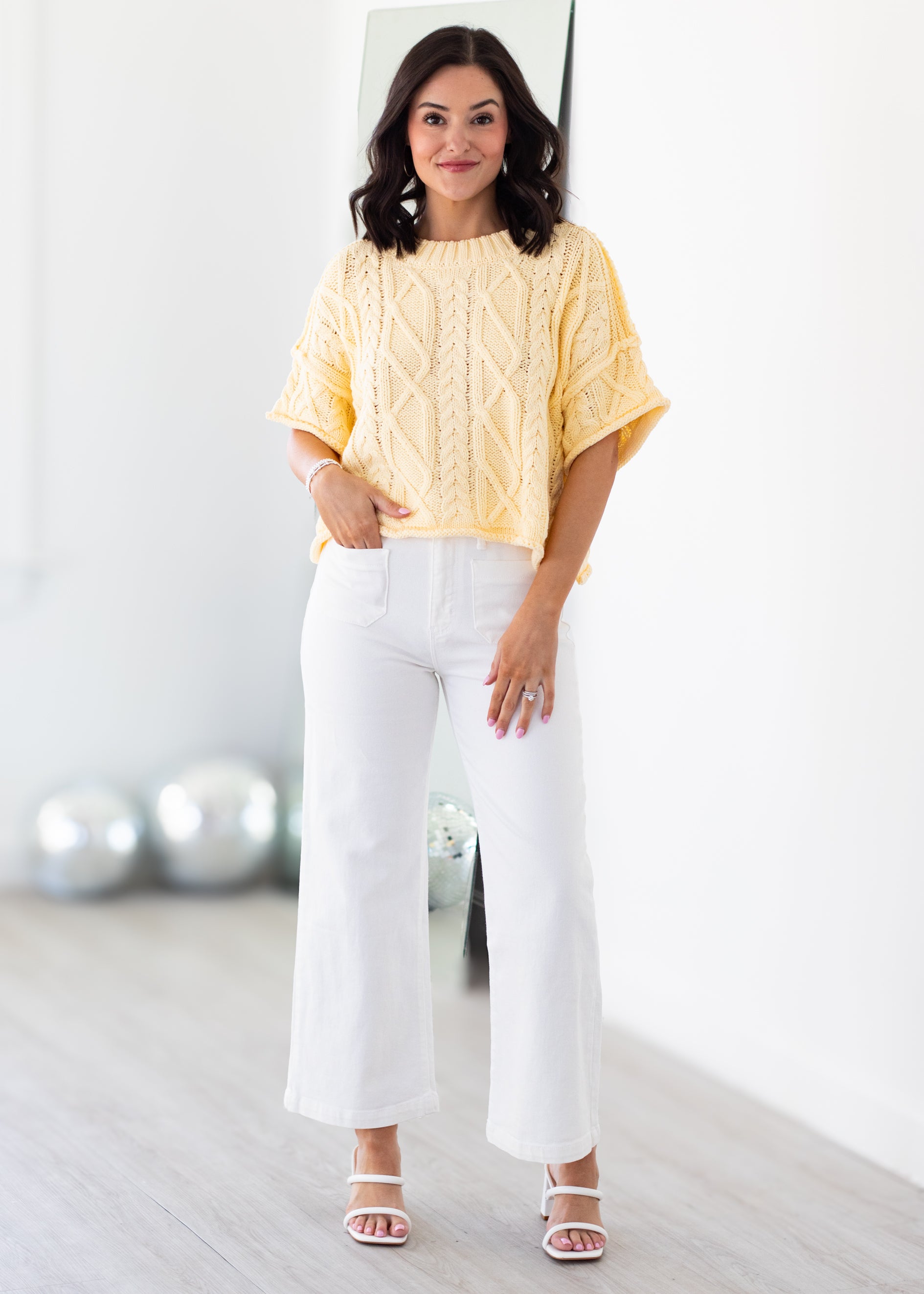 Woman wearing a yellow top and white pants in a minimalistic room.