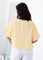 Woman wearing a yellow knitted top with a white background