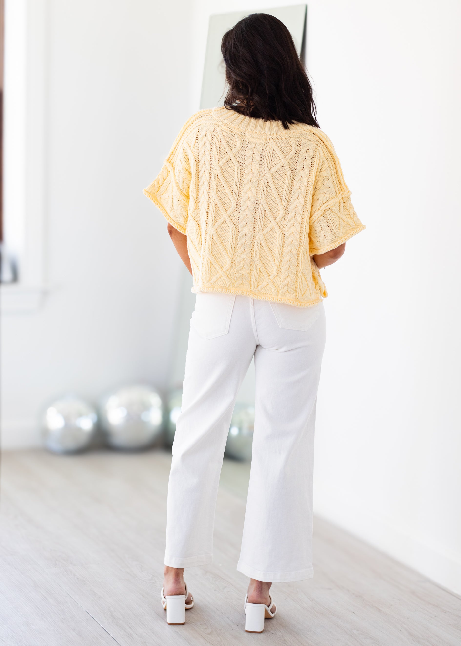 Woman wearing a yellow knitted sweater and white pants standing in front of a mirror.