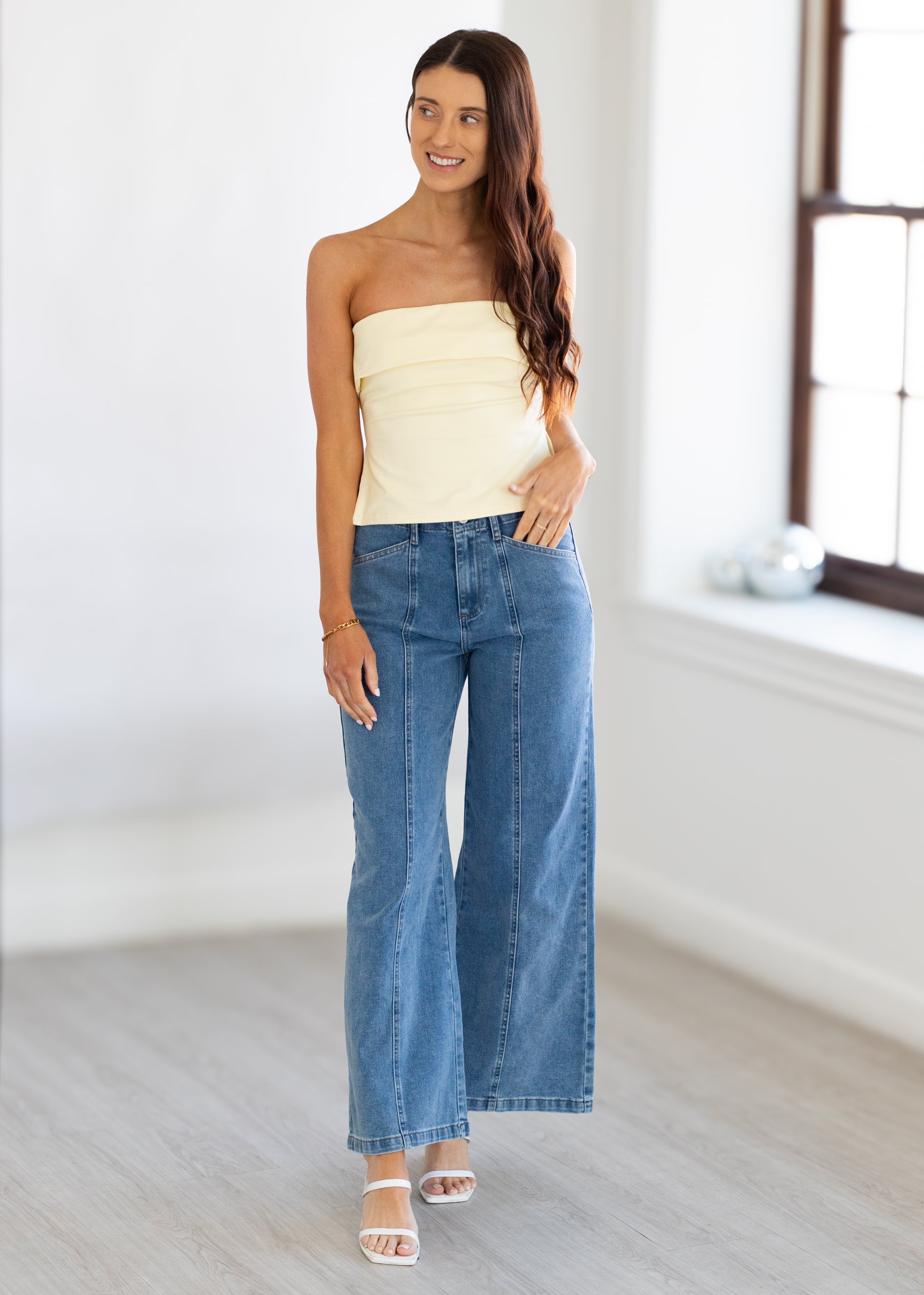 Woman wearing a strapless top and blue jeans in a bright room.