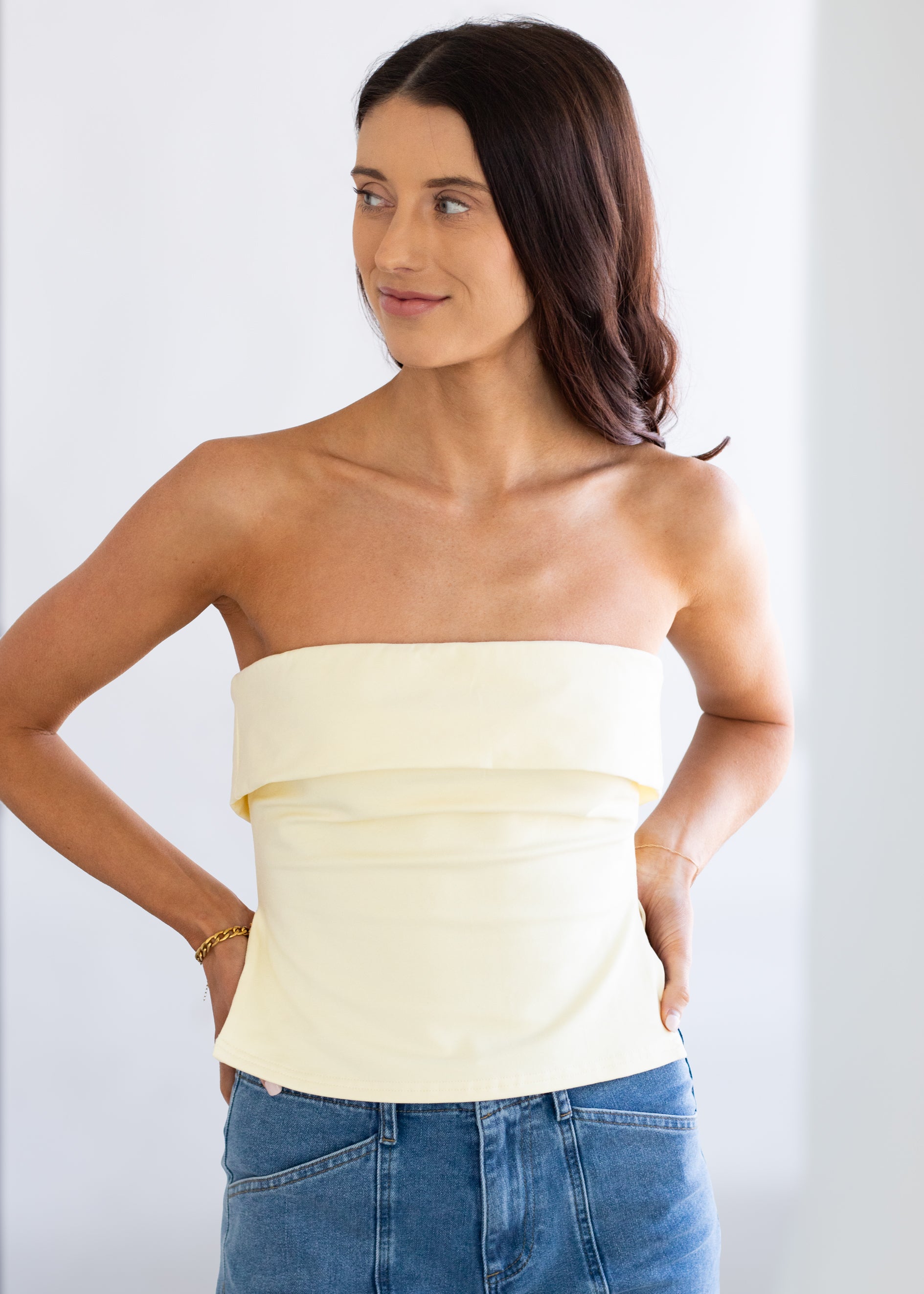 Woman wearing a strapless light yellow top and blue jeans against a white background