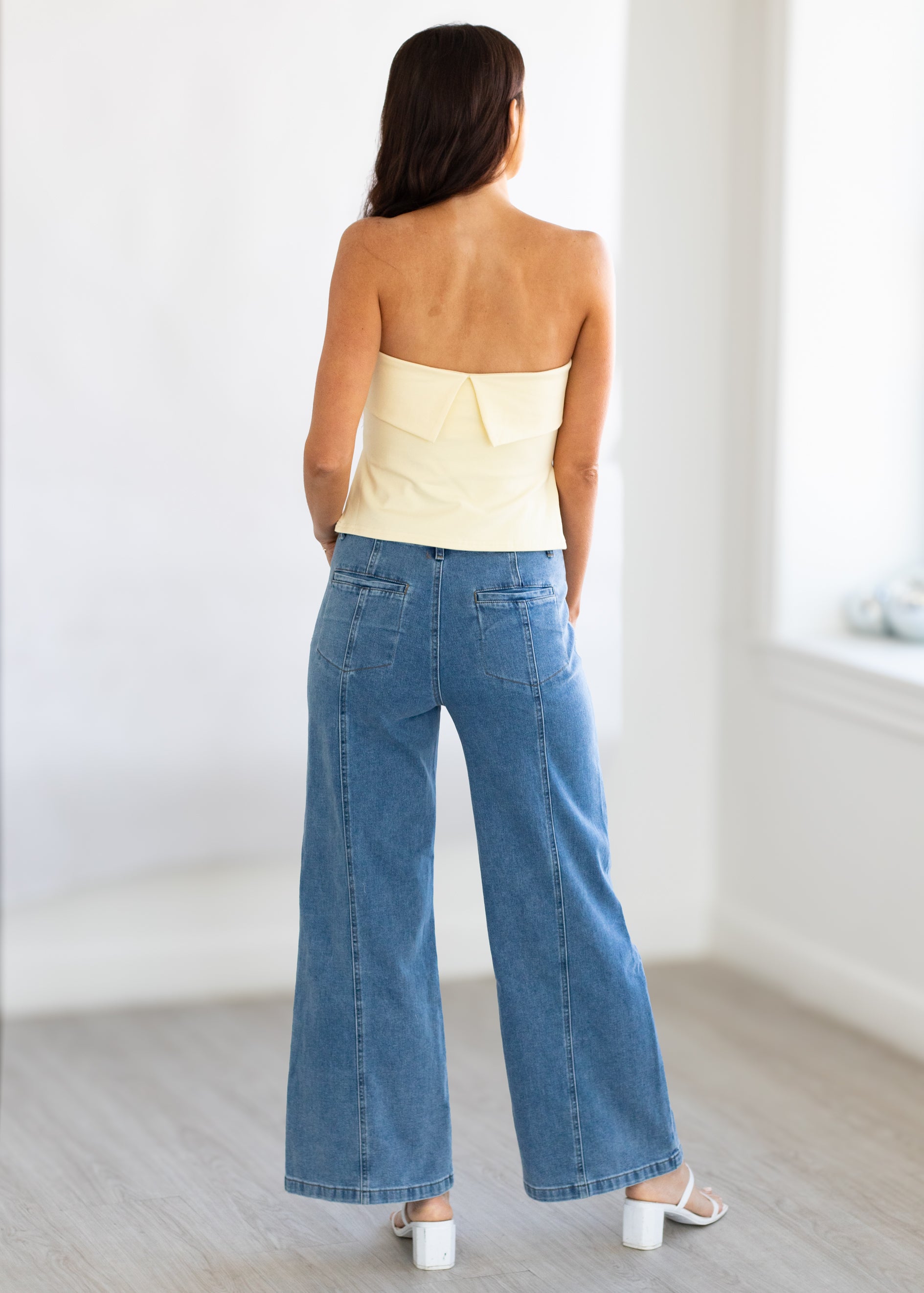 Woman wearing a strapless yellow top and blue jeans in a minimalistic room.