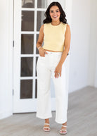 Woman wearing a yellow sleeveless top and white pants indoors.