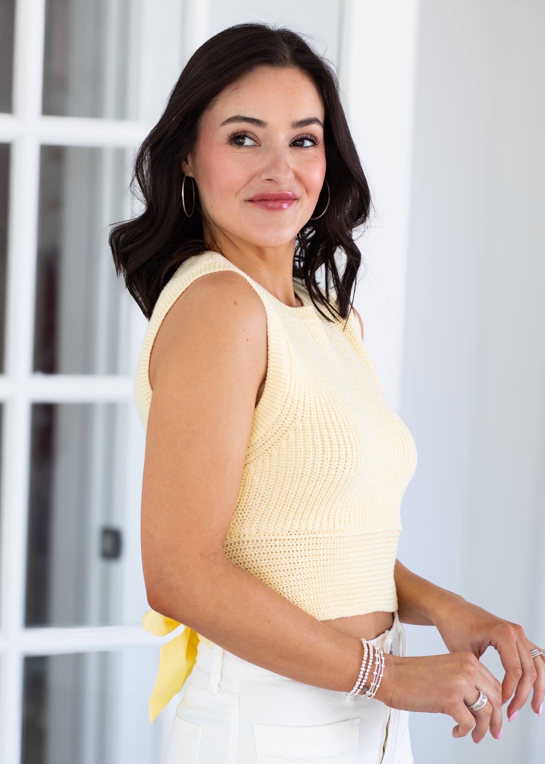 Woman wearing a yellow sleeveless top and white pants indoors.