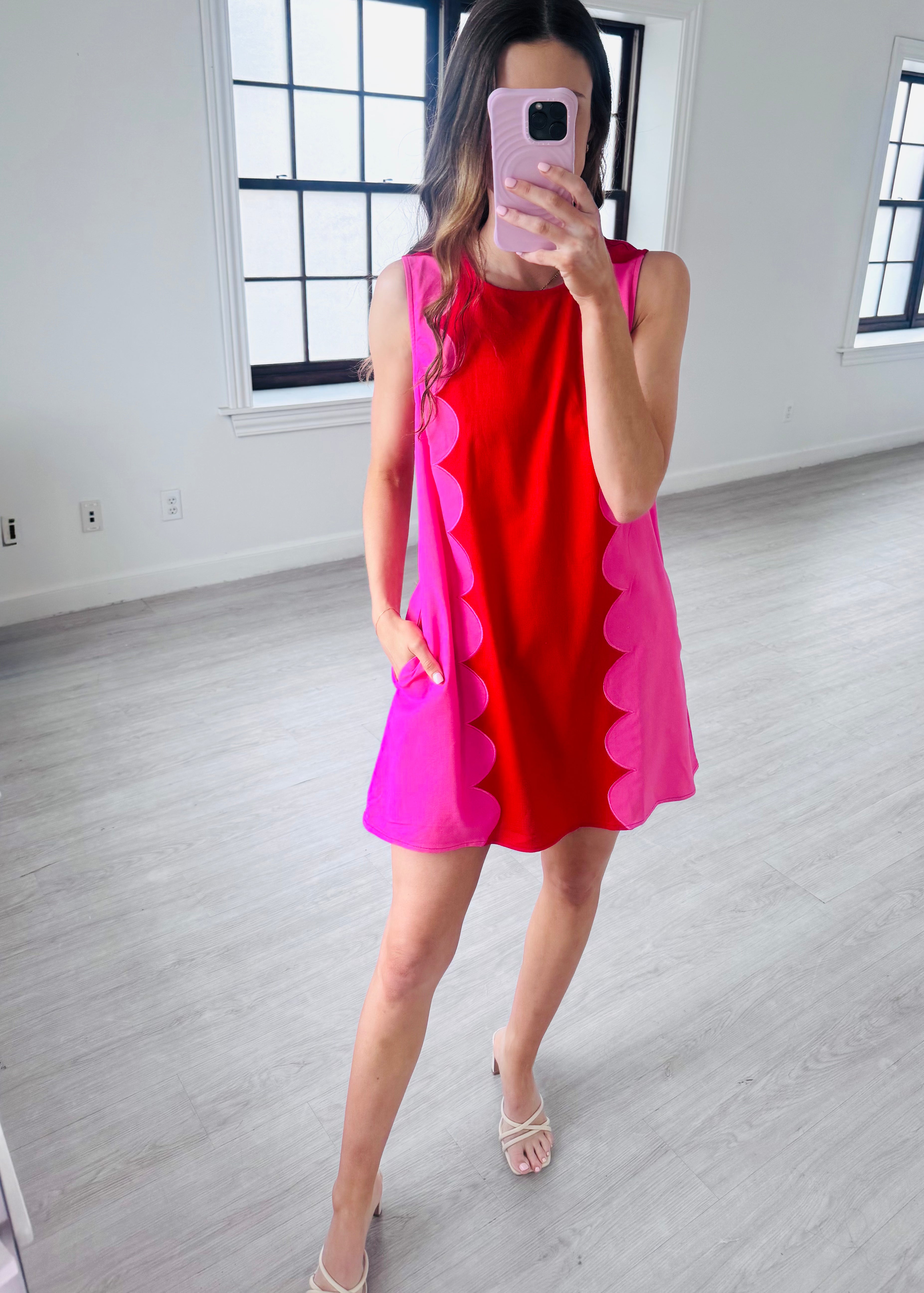 Woman taking a mirror selfie wearing a red and pink dress in a minimalistic room.