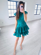 Woman taking a mirror selfie wearing a teal dress in a minimalistic room.