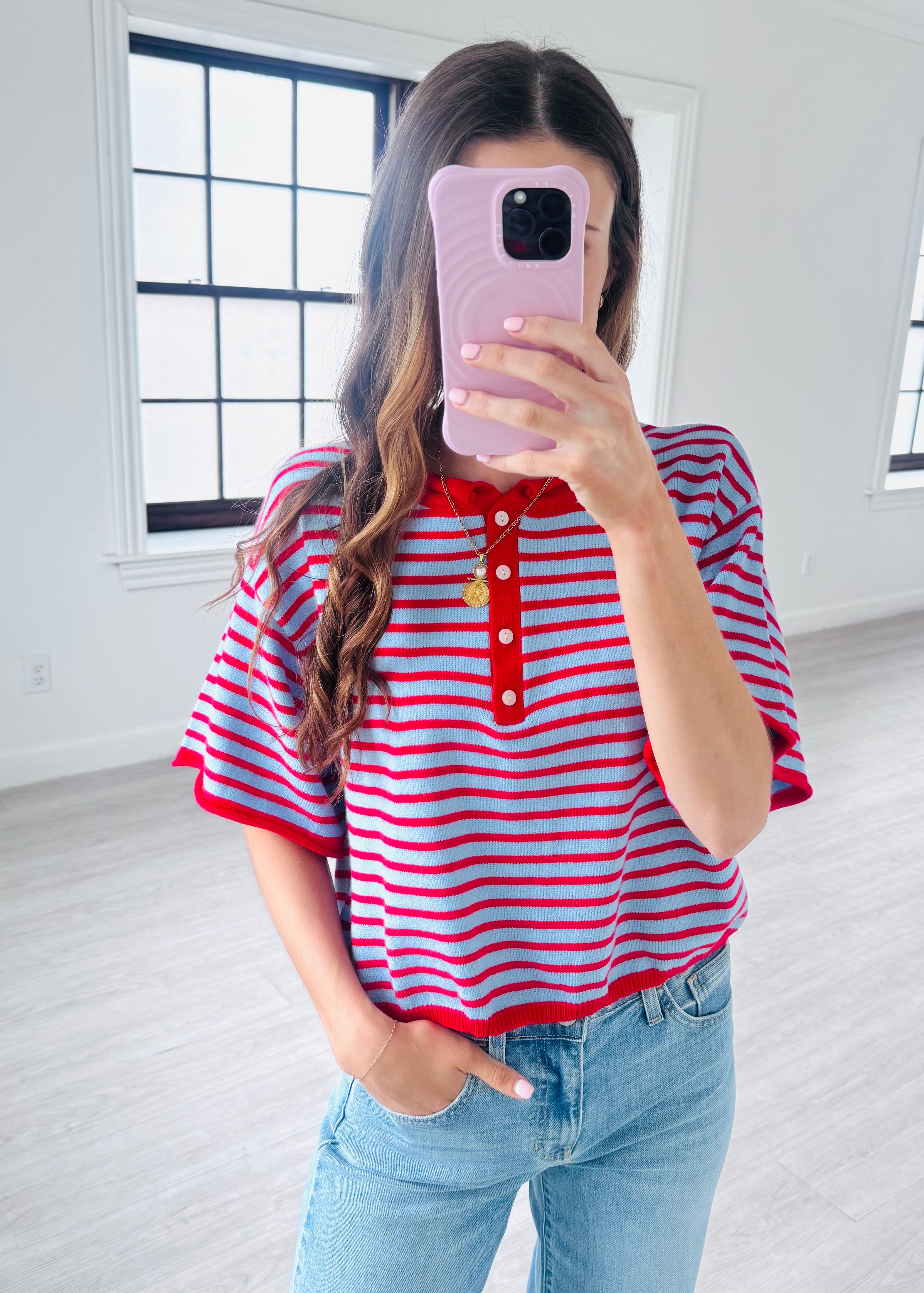 Person wearing a red and white striped shirt and blue jeans, taking a mirror selfie.