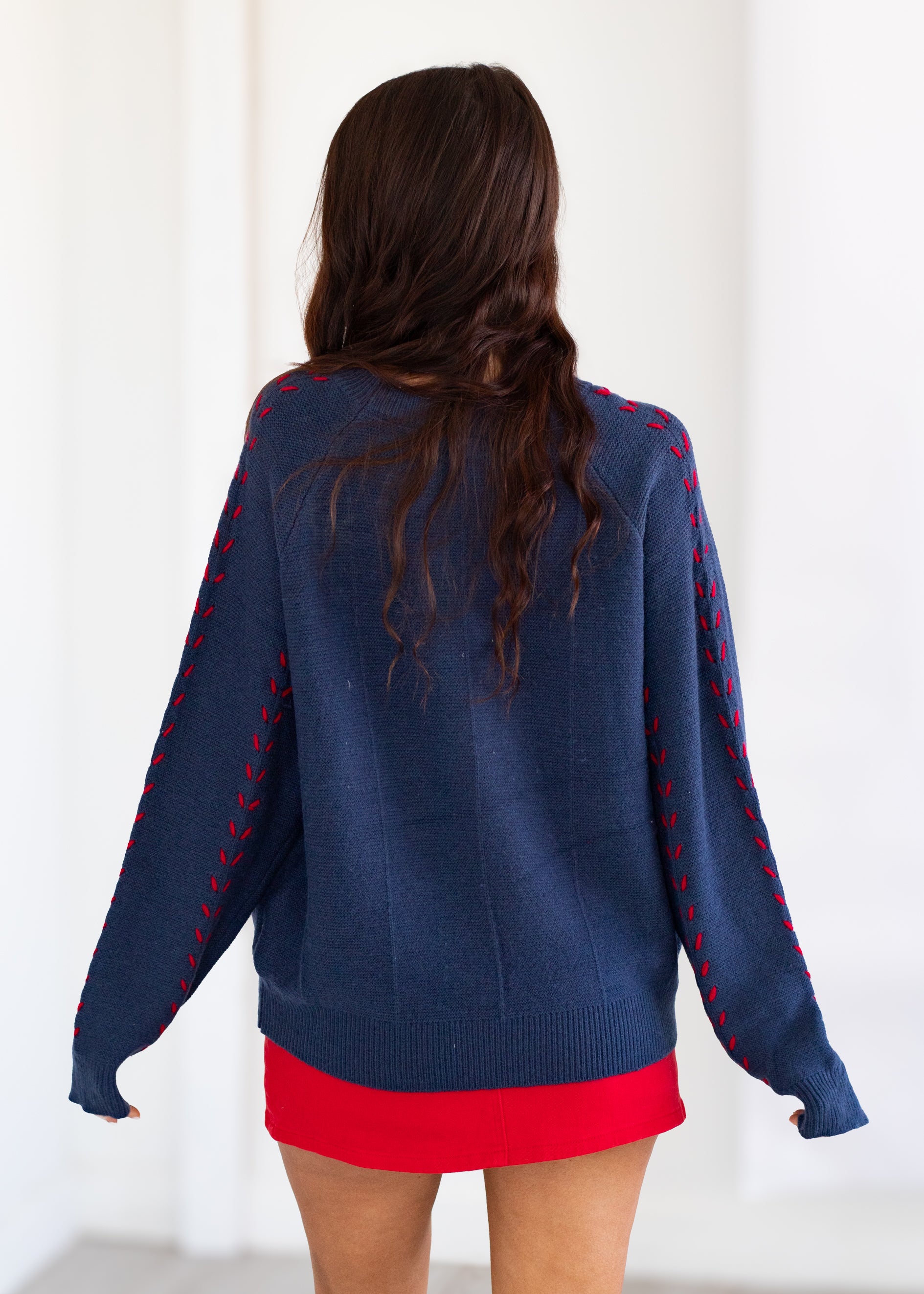 Person wearing a navy sweater with red accents on a white background