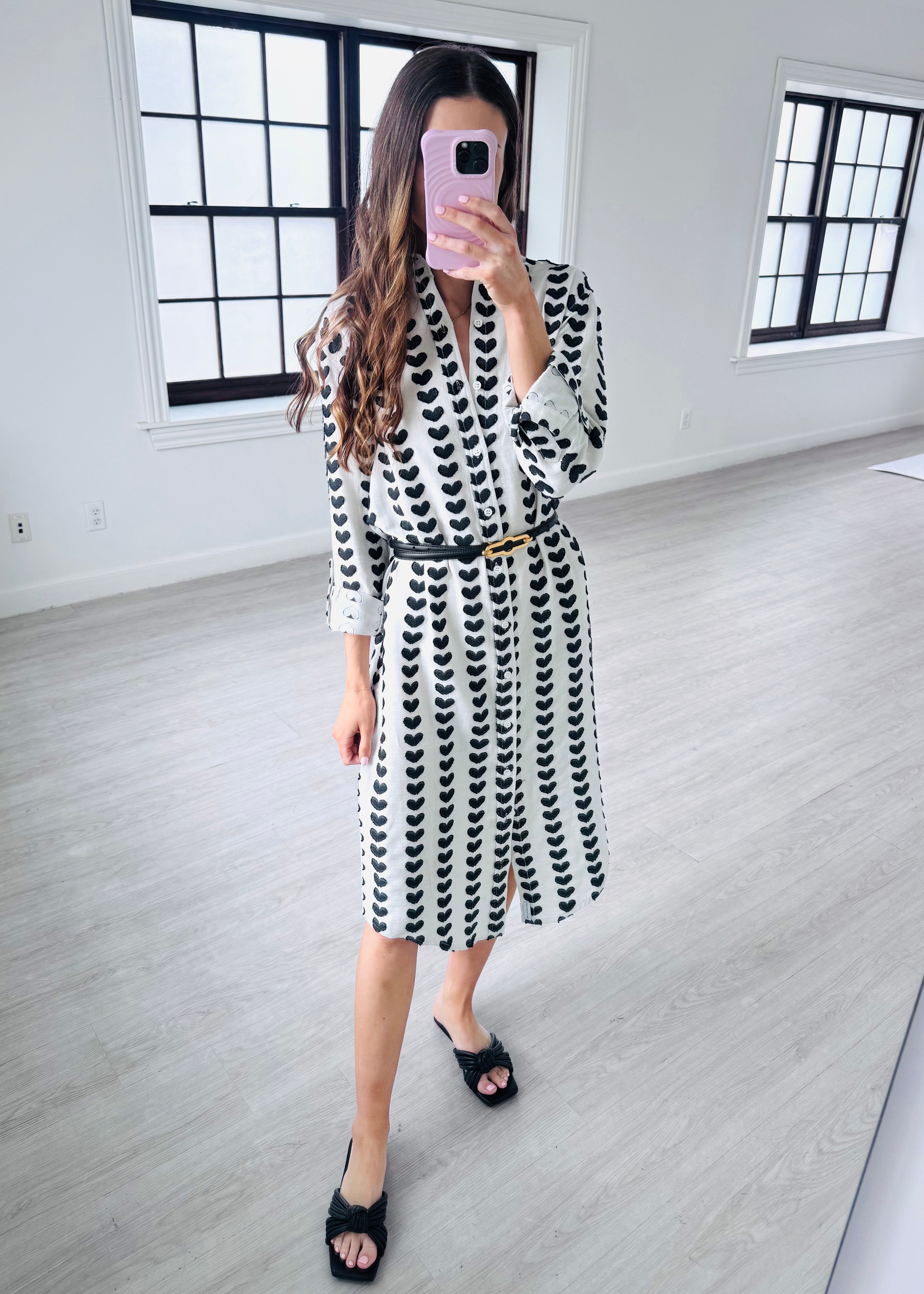 Woman taking a mirror selfie wearing a black and white patterned dress in a minimalistic room.