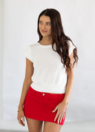Woman wearing a white top and red skirt against a plain background
