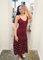 Woman taking a mirror selfie wearing a burgundy dress with white polka dots in a store.