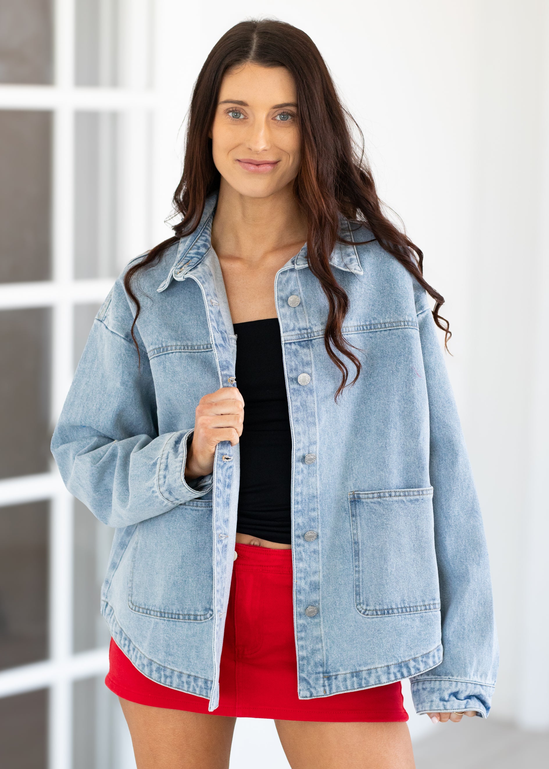 Woman wearing a light blue denim jacket over a black top and red skirt.