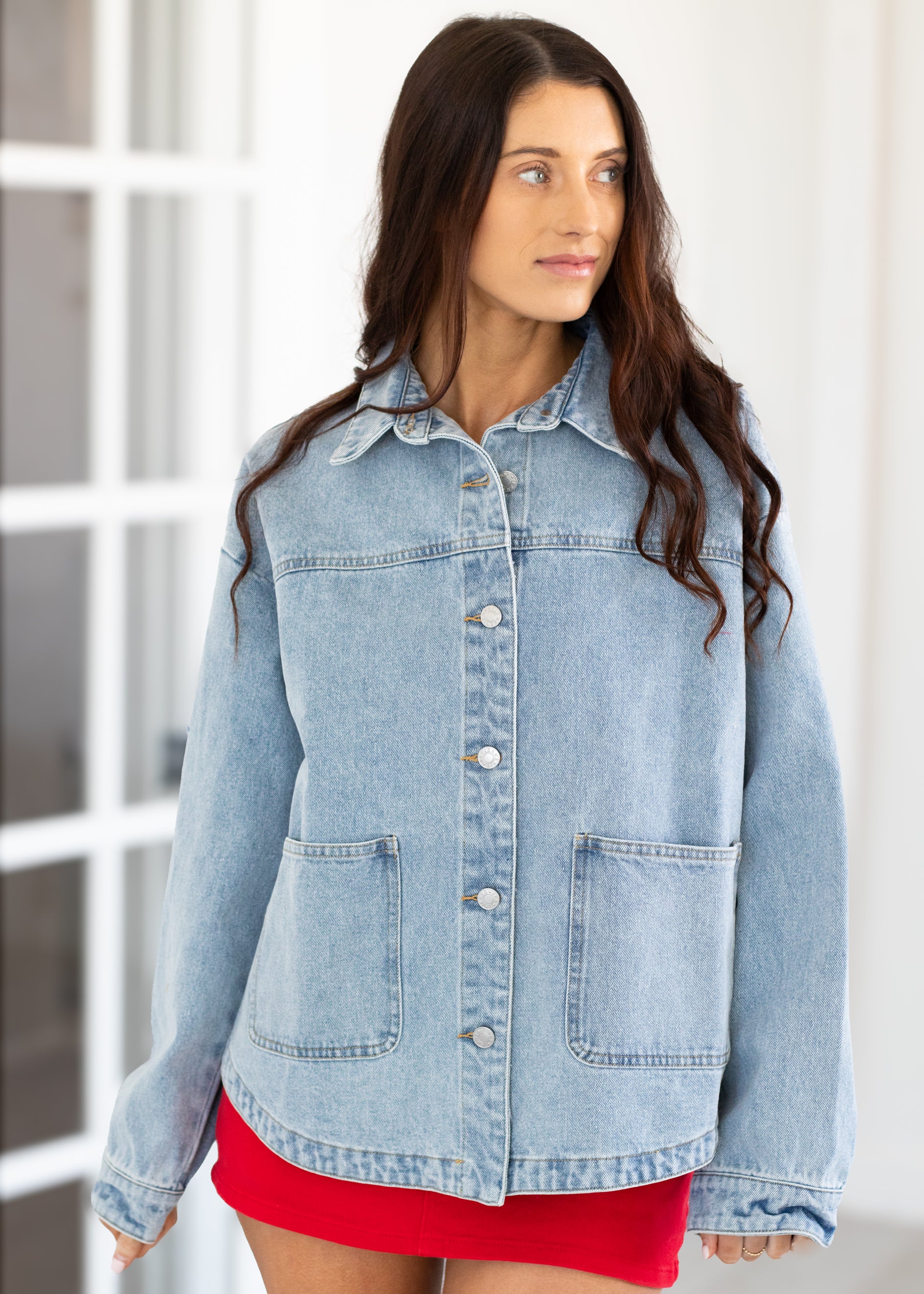 Woman wearing a light blue denim jacket over a red dress indoors.