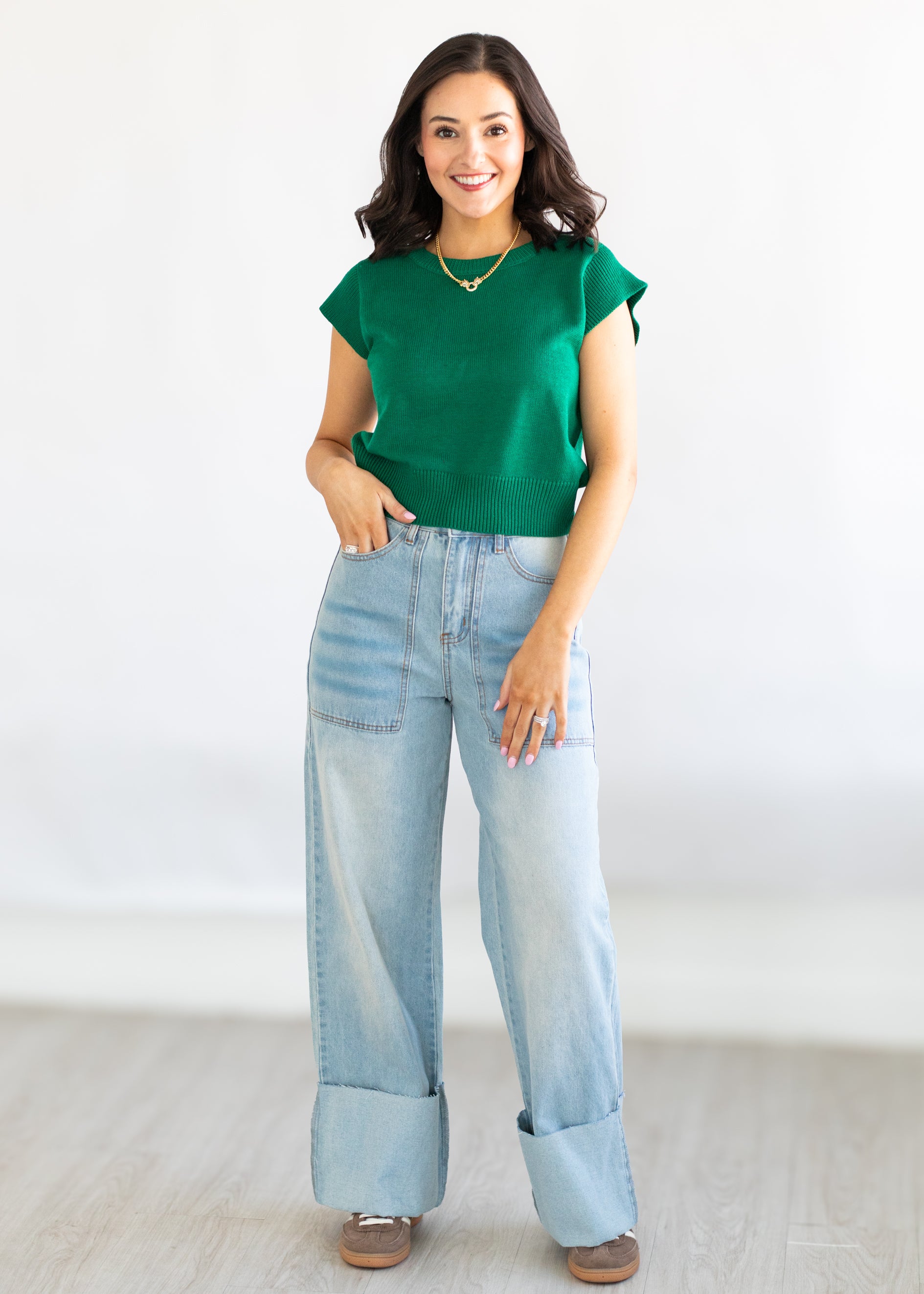 Woman wearing a green top and light blue jeans against a white background