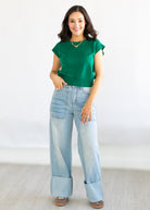 Woman wearing a green top and light blue jeans against a white background