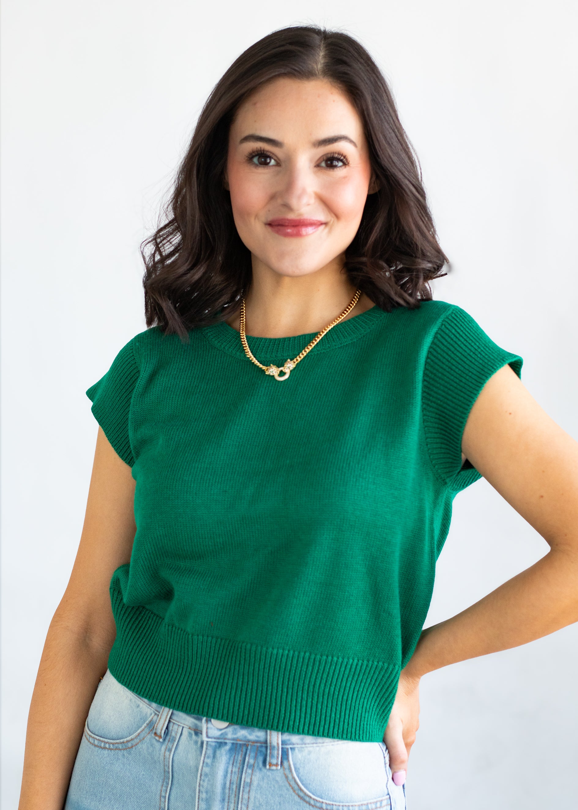 Woman wearing a green sweater and blue jeans against a white background