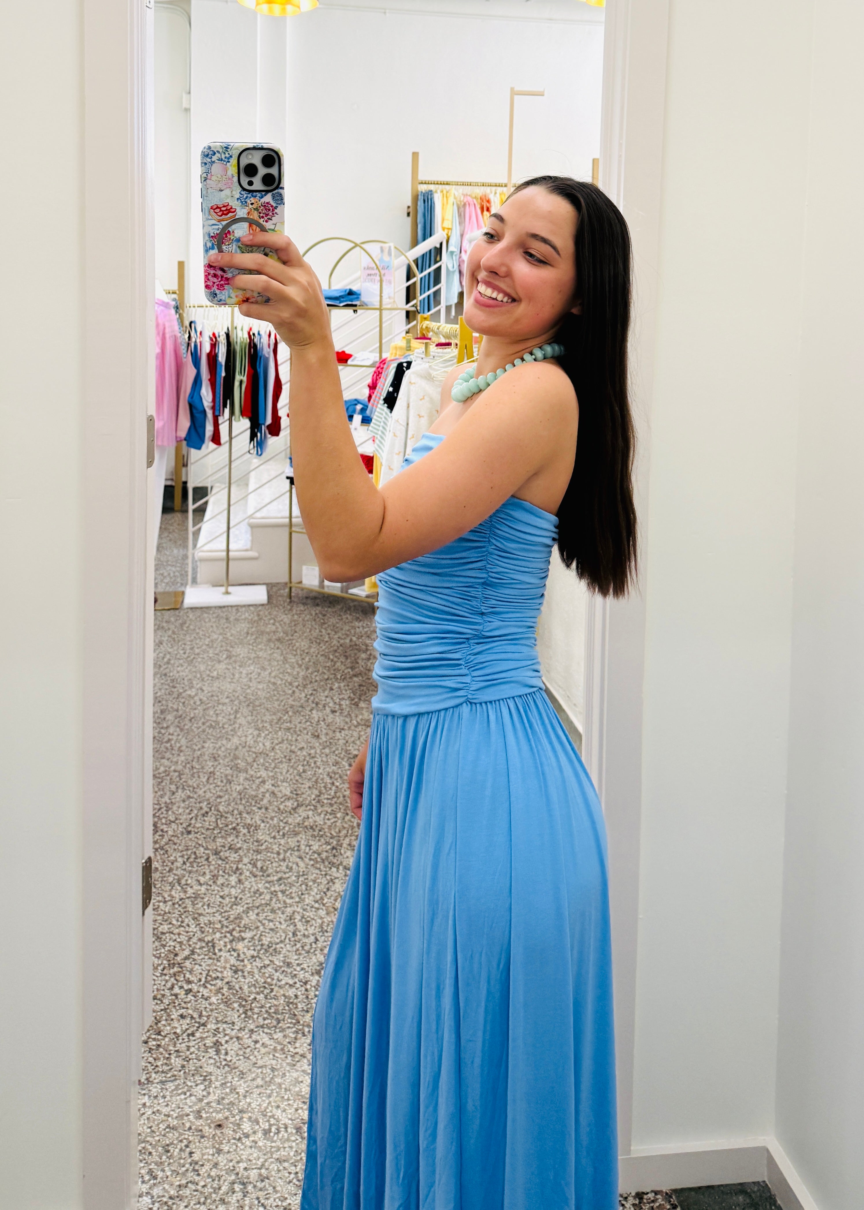 Woman taking a mirror selfie wearing a blue dress in a store.