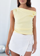 Woman wearing a yellow off-shoulder top and white skirt against a light background