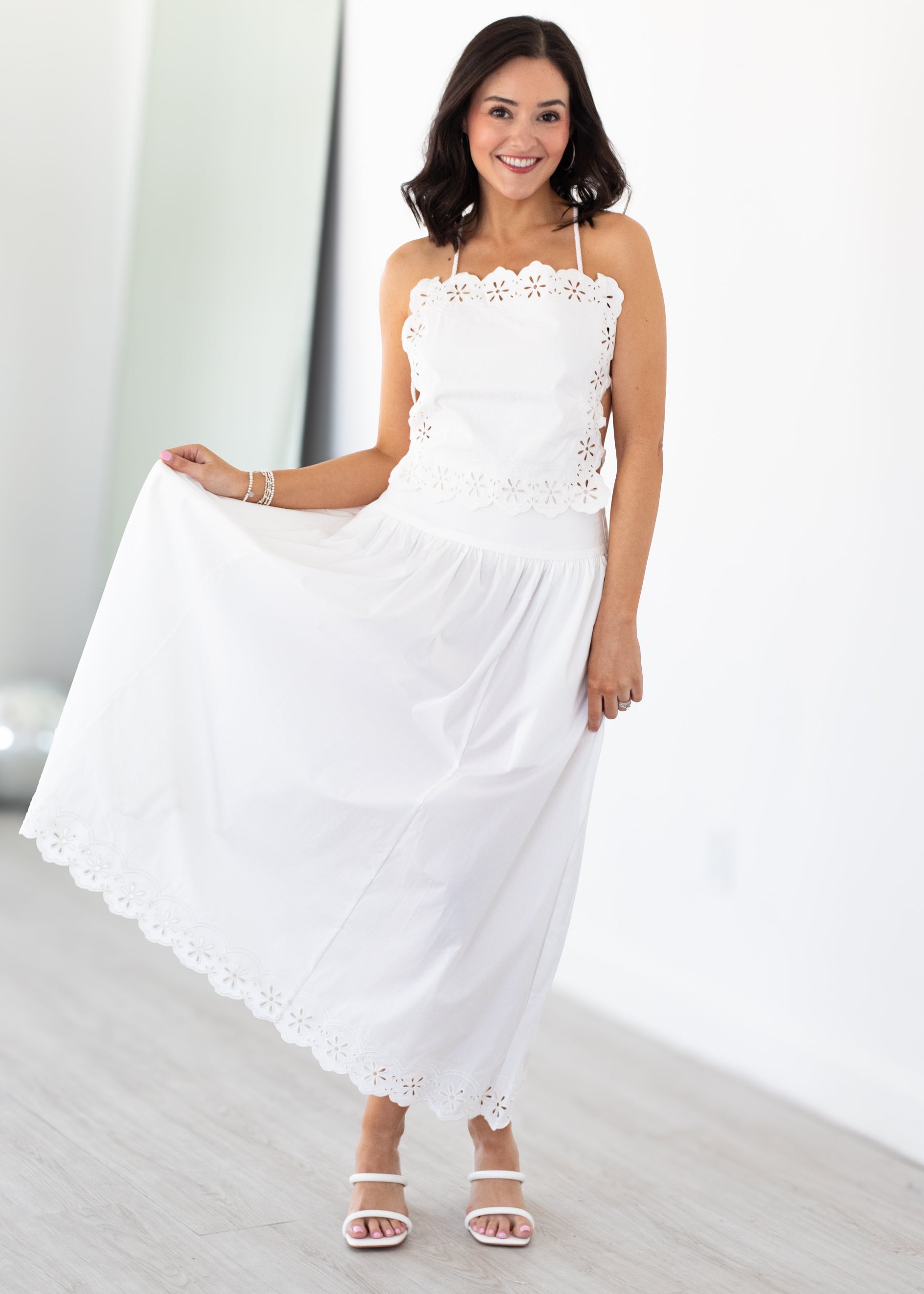 Woman wearing a white matching top and skirt set with lace details in a minimal indoor setting
