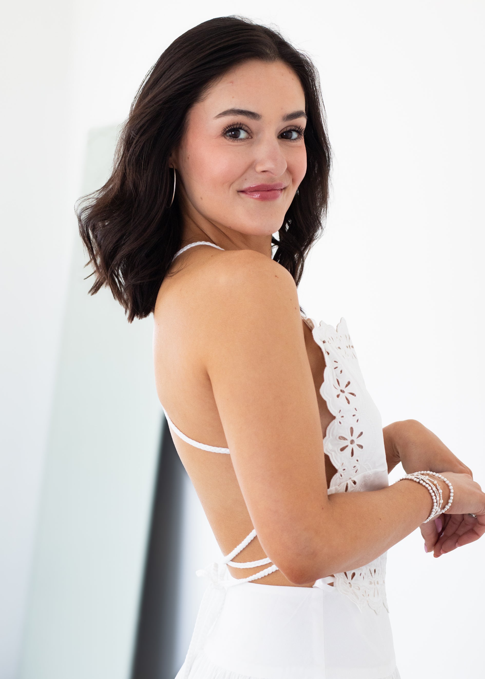 Woman wearing a white lace skirt and top set with thin straps on a plain background