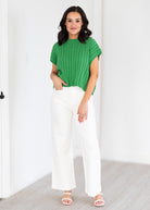 Woman wearing a green sweater and white pants in a minimal indoor setting