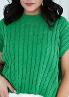 Green cable knit sweater worn by a person against a white background