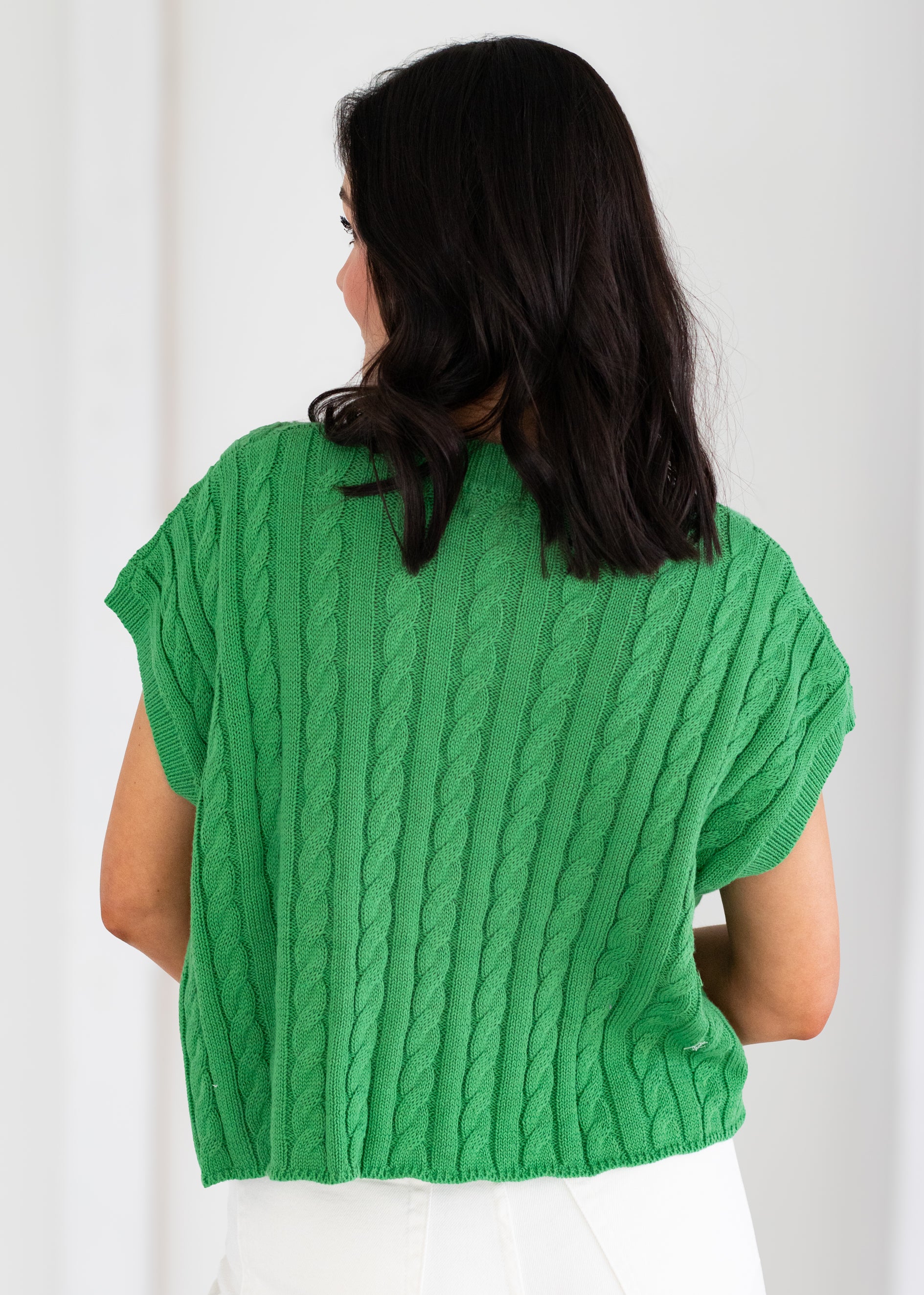 Person wearing a green cable knit sweater against a white background