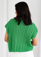 Person wearing a green cable knit sweater against a white background