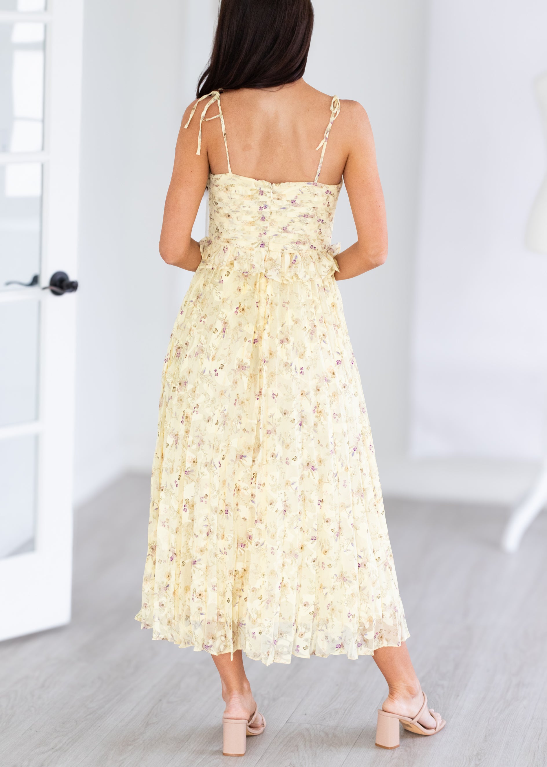 Woman wearing a yellow floral dress in a minimal indoor setting