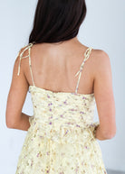 Woman wearing a light yellow floral dress with thin straps against a plain background