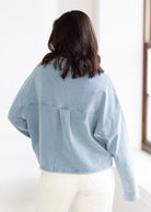 Person wearing a light blue denim jacket in a minimal indoor setting