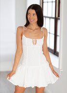 Woman wearing a white dress with thin straps in a bright room.