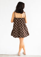 Woman wearing a brown dress with white polka dots on a white background